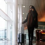 Woman walking with suitcase in the airport while using the mobile.