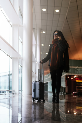 Woman walking with suitcase in the airport while using the mobile.